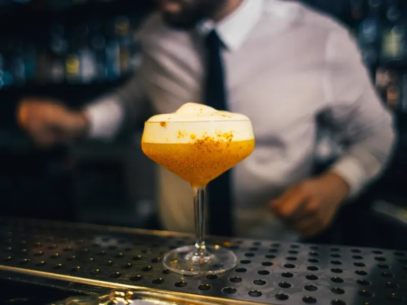 Bartender de gravata finalizando drink com espuma sobre o balcão