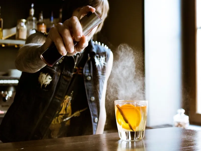 Bartender aplicando spray aromático sobre drink com casca de laranja